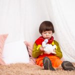 Adorable child sitting indoors with a toy, showcasing innocence and playfulness.