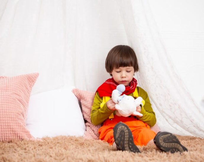 Adorable child sitting indoors with a toy, showcasing innocence and playfulness.