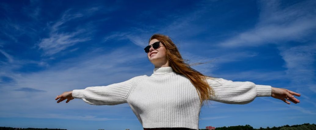 A woman with open arms and sunglasses enjoys the breeze at a beach in Tallinn, Estonia.